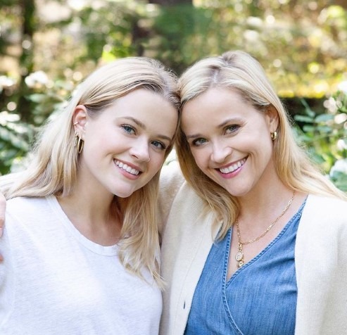 Reese Witherspoon tenant un livre, souriante, dans un cadre cosy