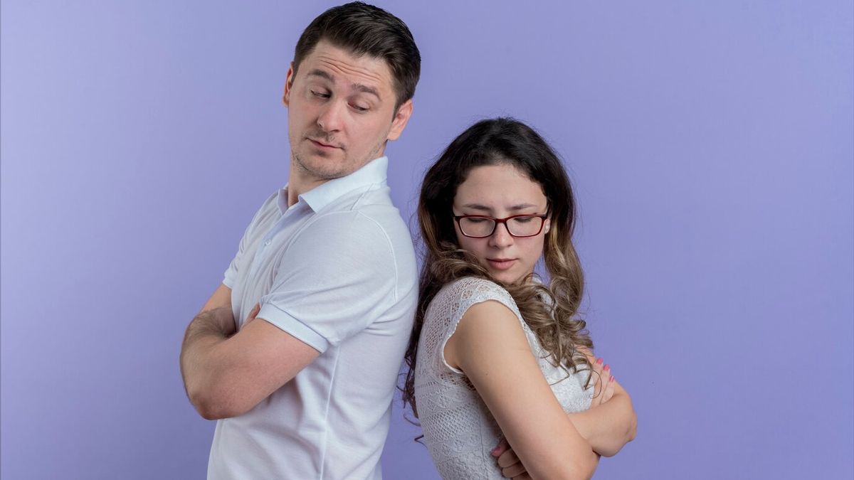 Femme regardant par la fenêtre, son partenaire dans le flou en arrière-plan, symbolisant l'isolement émotionnel