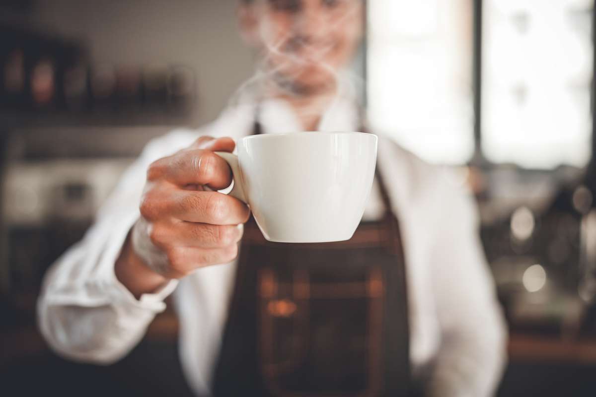 Personne versant du café fraîchement moulu dans une cafetière