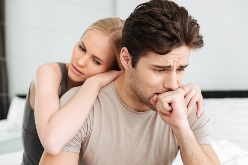 Couple assis sur un lit, la femme console son partenaire