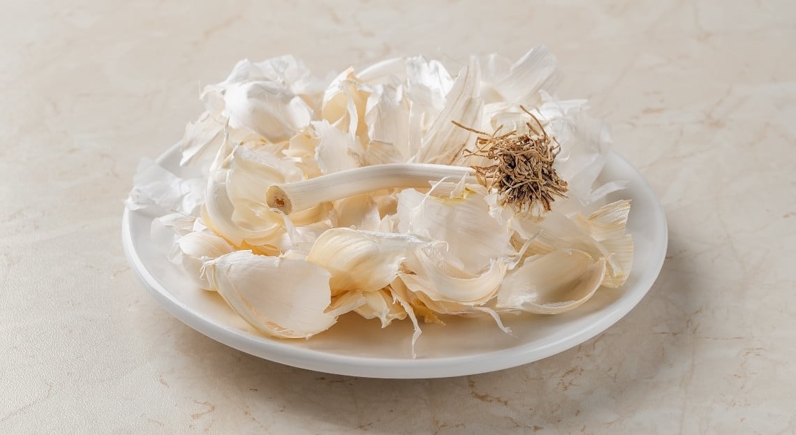 Des pelures d'ail dans un bocal en verre avec de l'eau, et un vaporisateur à côté